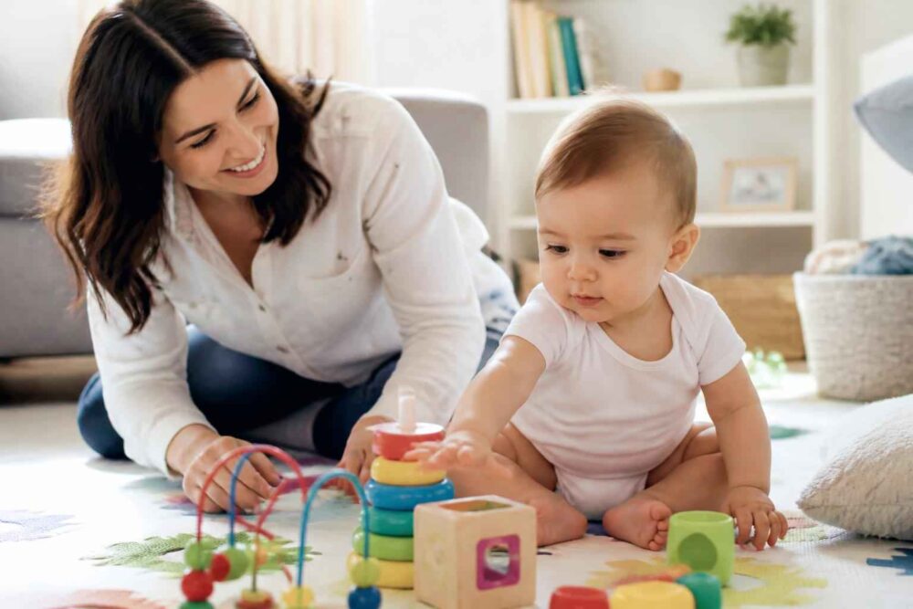 Mama i niemowlę bawią się kolorowymi klockami i zabawką zręcznościową na podłodze