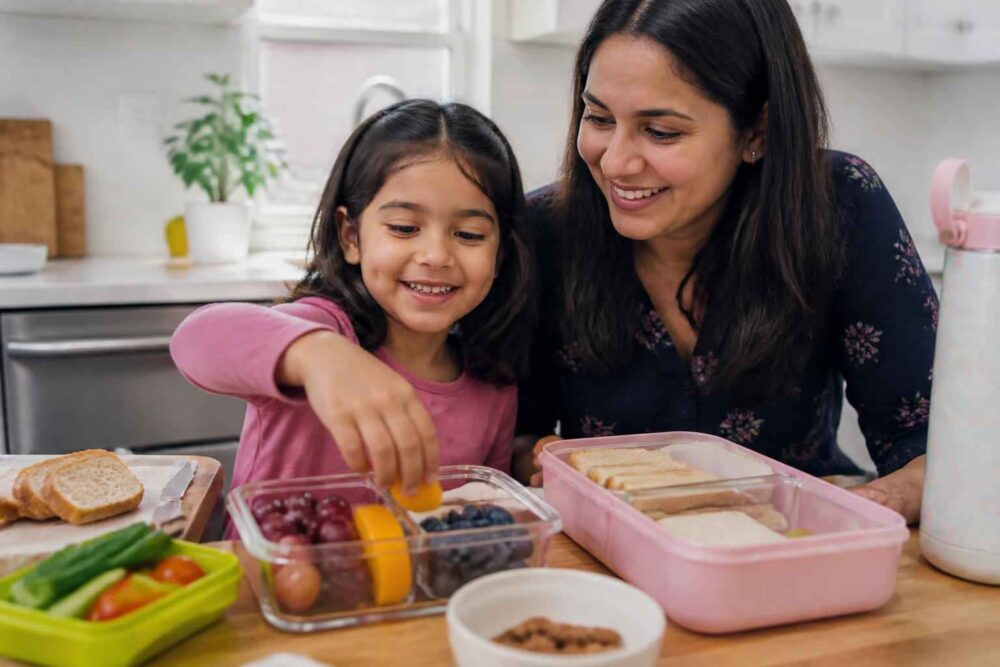 Mama i córka przygotowują lunch z kanapkami, owocami i warzywami w kuchni