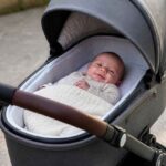 Noworodek owinięty w kocyk leży w gondoli wózka dziecięcego na zewnątrz